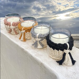 Peut inclure: Quatre bougies dans des pots en verre avec des housses en macramé de différentes couleurs. Les housses sont en corde naturelle et ont un pompon en bas. Les bougies sont blanches et les pots sont transparents.