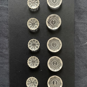 Puede incluir: Una colección de botones transparentes vintage. Cinco botones tienen un diseño festoneado en forma de flor con un agujero central. Cinco botones redondos presentan un intrincado patrón floral grabado con uno o dos agujeros. Todos los botones están sobre fondo negro.