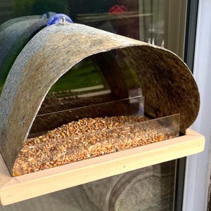 Peut inclure: Mangeoire &agrave; oiseaux en bois avec un toit incurv&eacute; en m&eacute;tal vieilli. La mangeoire a une fa&ccedil;ade en plastique transparent et est remplie de graines pour oiseaux. Elle est fix&eacute;e &agrave; une fen&ecirc;tre avec des ventouses bleues.