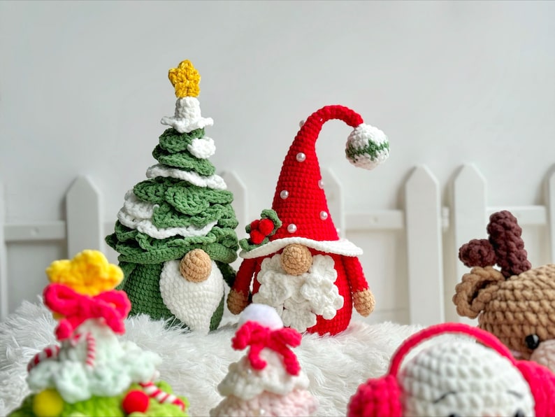 May include: A collection of crocheted Christmas ornaments, including a green Christmas tree, a red gnome, a white reindeer, and a white snowman. The ornaments are all handmade and feature intricate details.