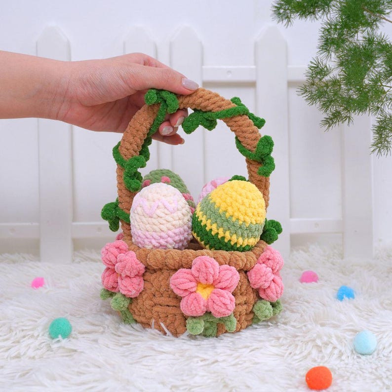 May include: A brown crocheted basket with a green vine handle and pink flowers. The basket is filled with three crocheted Easter eggs, one pink and white, one yellow and green, and one green and yellow.