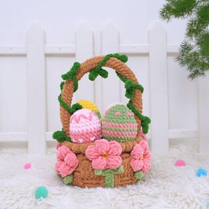 May include: A crocheted Easter basket with a brown handle and pink flowers. The basket is filled with three crocheted eggs in pink, green, and yellow.
