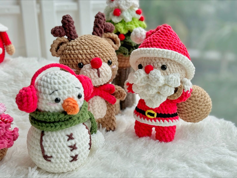 May include: Crocheted Christmas ornaments, including a snowman with a green scarf and red earmuffs, a reindeer with brown fur and red antlers, and a Santa Claus with a white beard and red suit.