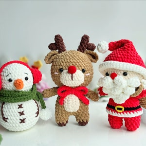 May include: Three crocheted Christmas ornaments: a snowman with a green scarf and red earmuffs, a reindeer with a red bow, and Santa Claus with a white beard and a red bag.