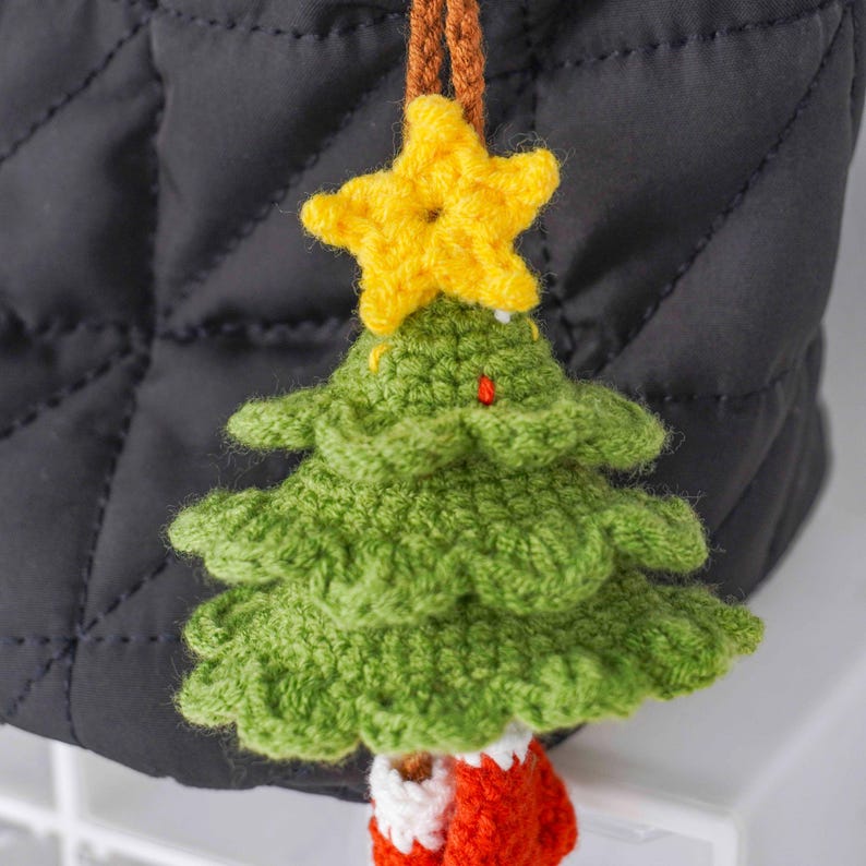Op de afbeelding: Een handgemaakte kerstboomversiering. De groene boom heeft een gele ster en een rood-witte sok. Hij hangt aan een bruin touwtje. Deze handgemaakte versiering is ideaal voor feestelijke decoraties.