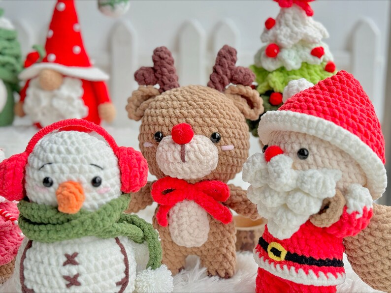 May include: A set of crocheted Christmas ornaments featuring a snowman with a green scarf and red earmuffs, a reindeer with red antlers and a red bow, and Santa Claus with a white beard and red hat.