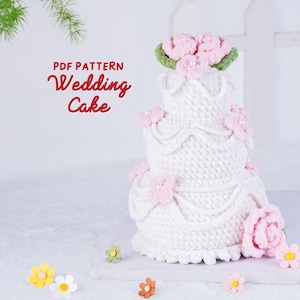 May include: A three-tiered white crocheted wedding cake with pink floral accents and a green leaf base. The cake is decorated with pearls and bows. The text "PDF PATTERN Wedding Cake" is in the upper left corner. Decorative flowers are scattered around the base.