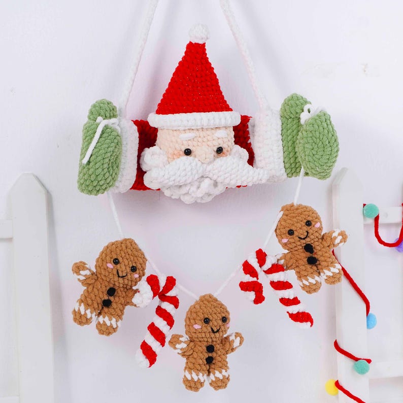 May include: A handmade Christmas decoration featuring a crocheted Santa Claus with a red hat and white beard, holding green mittens. Below, a garland of gingerbread men and candy canes hangs from a white string. The festive decor is perfect for the holiday season.