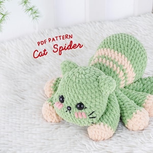 Puede incluir: Un peluche Cat Spider tejido a ganchillo en verde y rosa. El peluche tiene una cabeza de gato con mejillas rosas y ojos negros, y patas de araña. El texto "PDF PATTERN Cat Spider" es rojo.