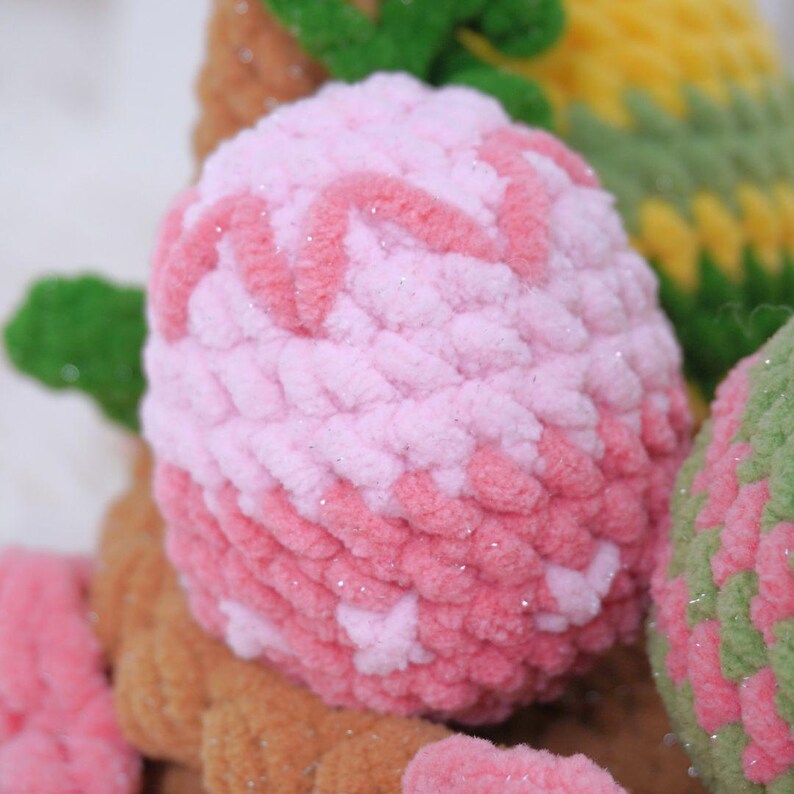 May include: A pink and white crocheted Easter egg with a sparkly finish. The egg is made with a textured yarn and has a soft, fluffy appearance.