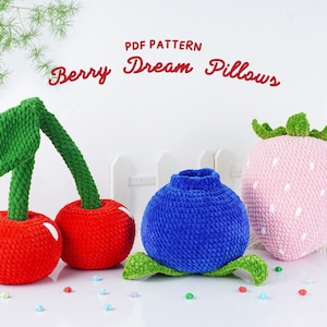 Puede incluir: Un conjunto de almohadas de ganchillo hechas a mano con forma de frutas. El conjunto incluye dos cerezas rojas con tallos verdes, un arándano azul y una fresa rosa con semillas blancas y un tallo verde. El texto "Berry Dream Pillows" está encima.