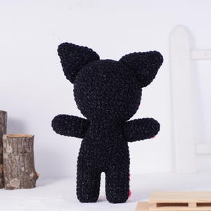 May include: A handmade black plush cat toy with large ears and outstretched arms. The cat has pink accents on its paws. The toy is made of a textured, sparkly material and stands upright.