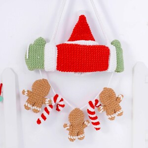 May include: A handmade Christmas decoration featuring a red and white Santa hat and a red and white candy cane design. Below, a garland of gingerbread men and candy canes hangs from the main decoration. The decoration is made of yarn.