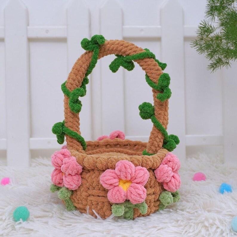 May include: A brown yarn basket with pink flowers and green vines around the handle. The basket is sitting on a white fluffy surface.