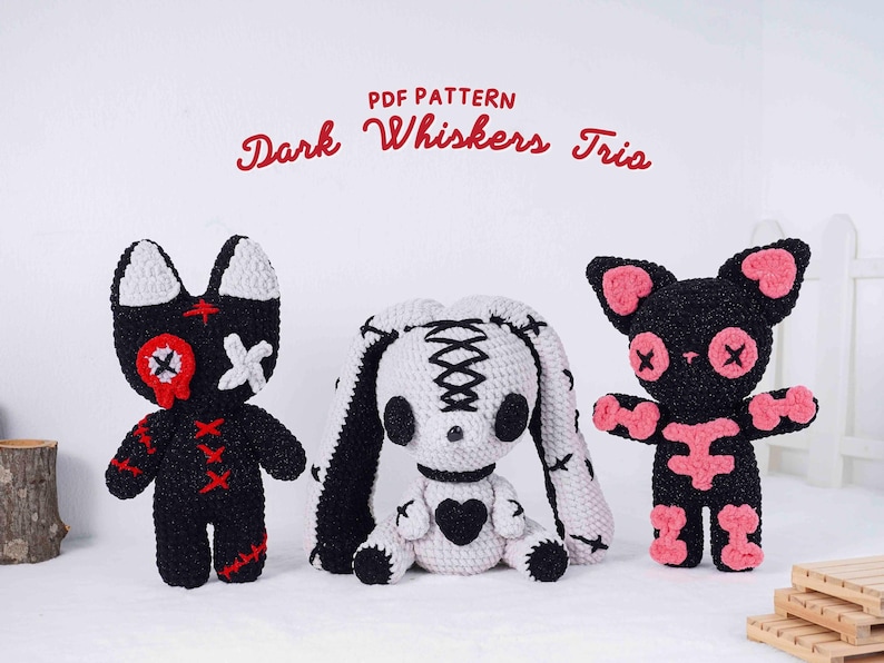 May include: Three crocheted plush toys: a black cat with red accents, a white bunny with black stitching, and a black cat with pink accents. The text "PDF Pattern Dark Whiskers Trio" is in red script above the toys.
