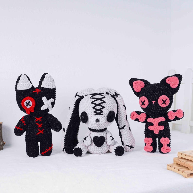 May include: Three handmade crochet dolls in a gothic style. The dolls include a black cat with pink accents, a white bunny with black details, and a black cat with red accents. Each doll has stitched details and a unique design.