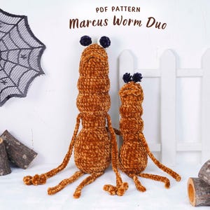 Puede incluir: Dos gusanos de peluche marrones con extremidades largas y antenas de pompón azul oscuro. El gusano más grande está al lado de uno más pequeño. El texto "PDF PATTERN Marcus Worm Duo" está en la parte superior. Una telaraña decorativa y rodajas de madera están en el fondo.