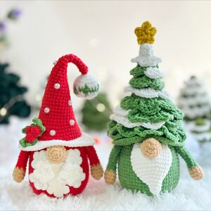 May include: Two crocheted Christmas gnomes, one dressed as a red and white gnome with a holly sprig and the other dressed as a green and white Christmas tree gnome with a gold star.