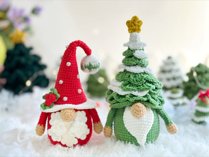 May include: Two crocheted Christmas gnomes, one dressed as a red and white gnome with a holly sprig and the other dressed as a green and white Christmas tree gnome with a gold star.