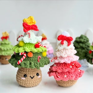 May include: A collection of handmade crocheted Christmas tree ornaments. The ornaments are made in various colors, including green, red, white, and pink. Each ornament features a cute face and is decorated with candy canes, beads, and pom-poms.