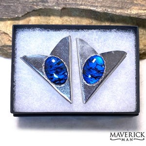May include: A pair of silver-toned cufflinks in a black box. Each cufflink has a triangular shape with a blue oval center. The blue centers have a marbled appearance. The cufflinks are presented on a white, textured surface.