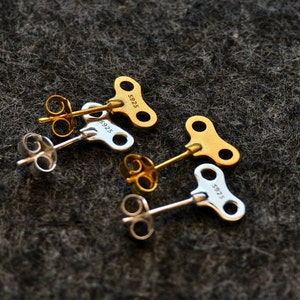 May include: Four silver and gold key-shaped earrings with a post and back. The earrings are marked with the number "5925".