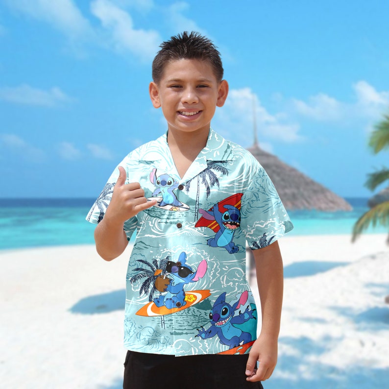 Op de afbeelding: Een lichtblauw overhemd met korte mouwen met een tropische print met Stitch van Lilo & Stitch. De print toont Stitch surfen op golven met palmbomen op de achtergrond.