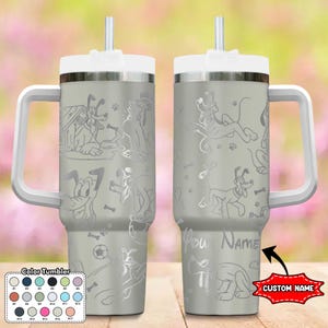 May include: A grey stainless steel travel mug with a white lid and handle. The mug features a design of a cartoon dog with a bone and a football. The mug has a straw and a space for a custom name.