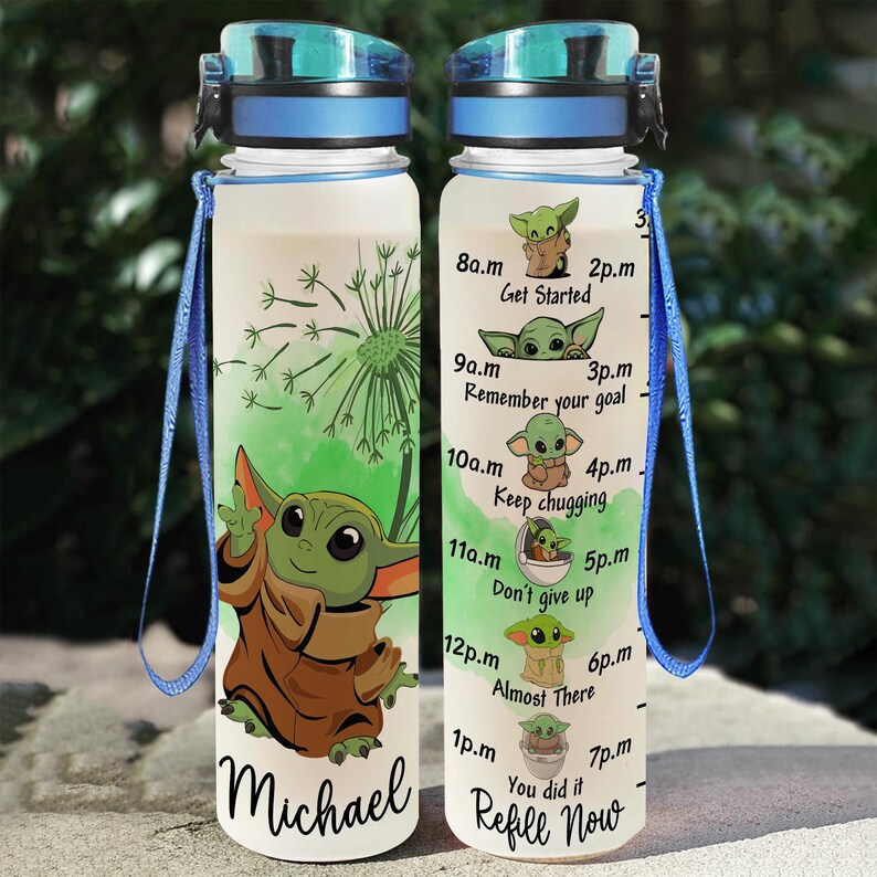 May include: A clear plastic water bottle with a blue lid and a blue carrying strap. The bottle has a green and white design with a cartoon character and motivational text. The text reads "8a.m Get Started" and continues with times and motivational phrases throughout the day. The bottle is personalized with the name "Michael" at the bottom.