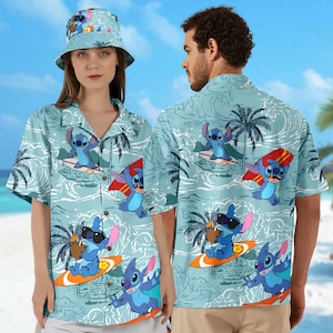 Op de afbeelding: Twee blauwe en witte Hawaiiaanse overhemden met een cartoonfiguur die op een golf surft. De overhemden hebben palmbomen en een blauwe oceaanachtergrond.