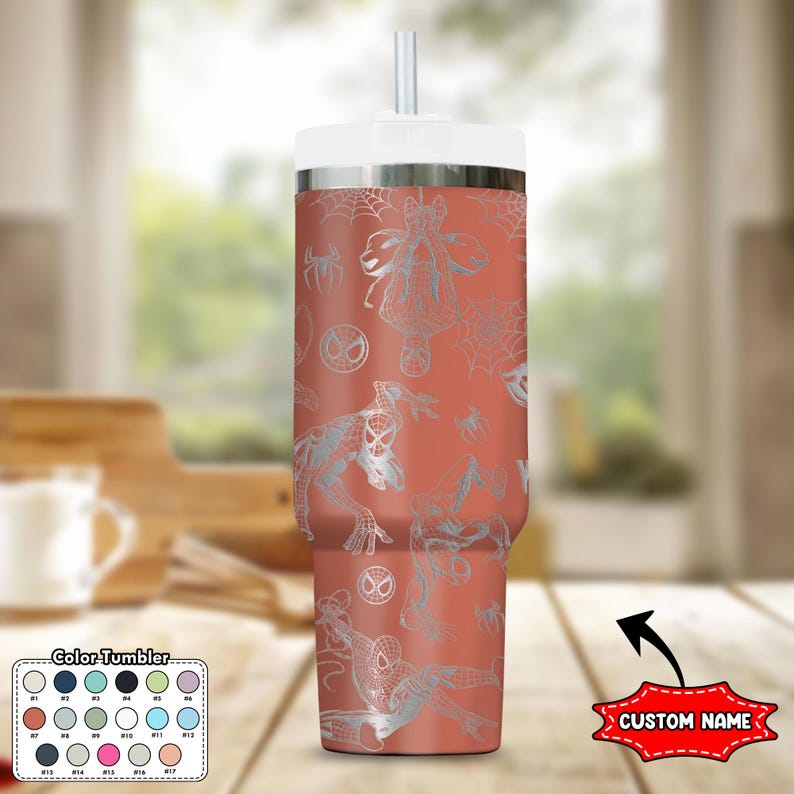 May include: A coral-colored tumbler with a white lid and straw, featuring a silver Spider-Man pattern. The design includes Spider-Man figures, spiderwebs, and the Spider-Man logo. The tumbler has a "Custom Name" label.