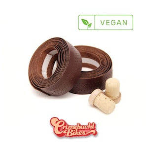 Könnte beinhalten: Zwei Rollen braunes veganes Lenkerband mit Kork-Lenkerendstopfen. Das Band hat eine strukturierte, perforierte Oberfläche. Die Verpackung enthält ein grünes Blatt mit dem Wort "VEGAN" darauf.