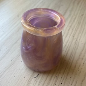 May include: A small, iridescent purple and gold vase with a swirling pattern. The vase has a smooth, rounded shape and a wide opening.