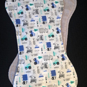 May include: A white burp cloth with a blue and green truck pattern. The cloth has the words "Bop Beep" and "Tat Toot" printed on it. The cloth is backed with a gray terry cloth.