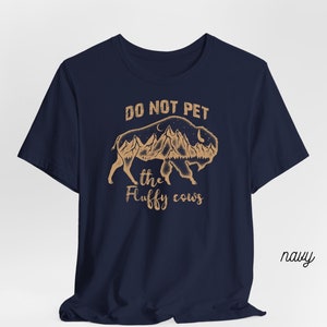 May include: Navy blue t-shirt with a brown graphic of a bison with mountains and the text "Do Not Pet the Fluffy Cows".