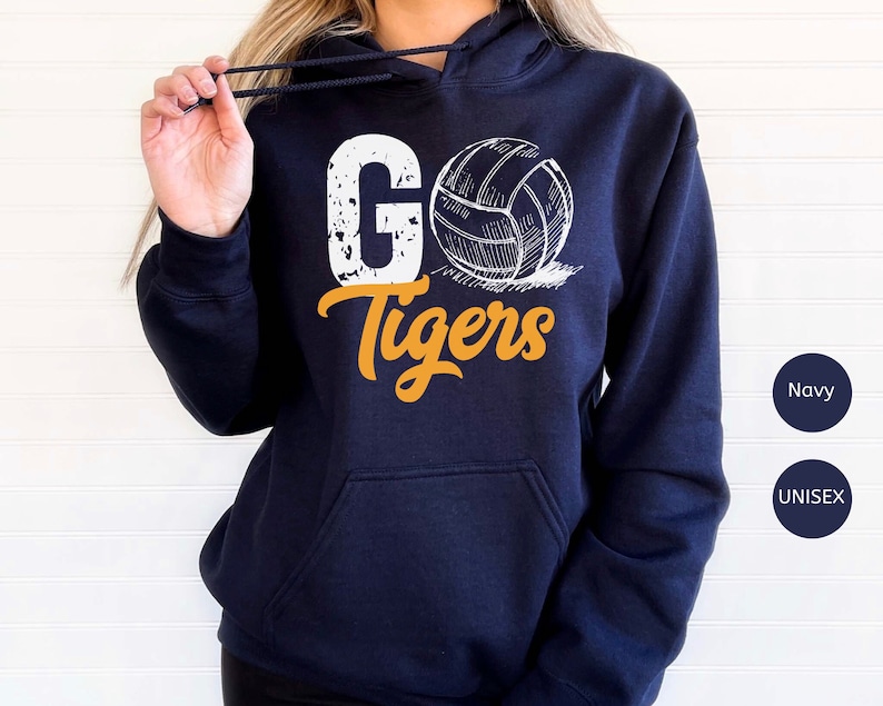 以下が含まれることがあります： 紺色のユニセックスフーディー。白いバレーボールとオレンジ色の「Go Tigers」の文字がプリントされています。