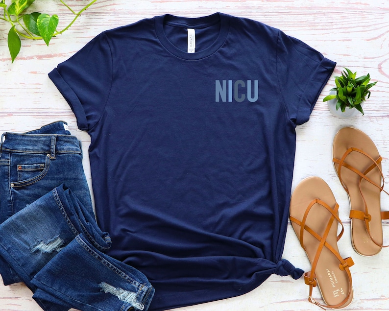 May include: A navy blue t-shirt with the word "NICU" printed on the front in a gradient of blue shades.
