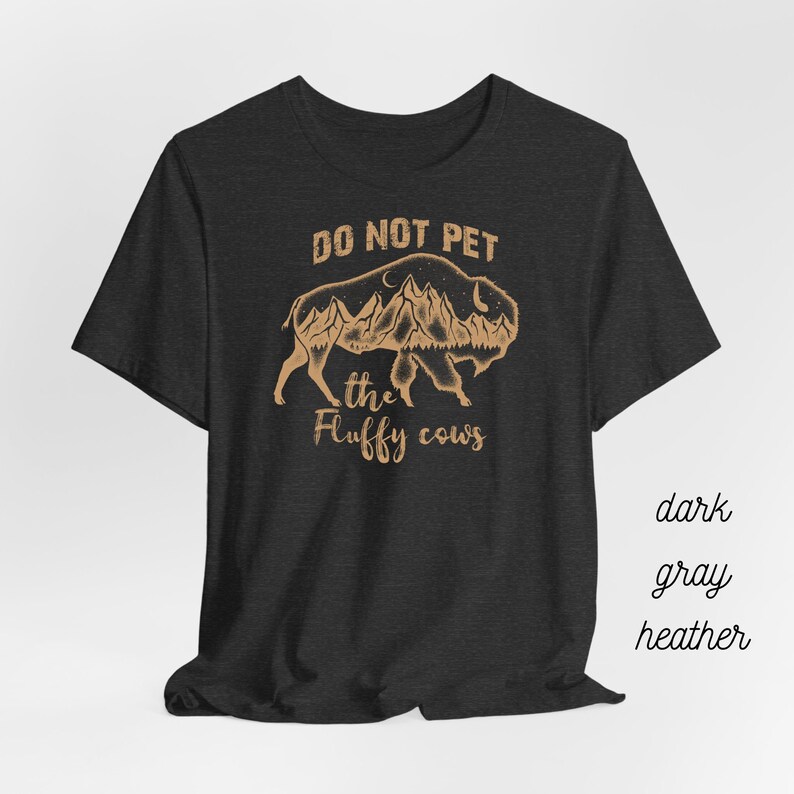 May include: Dark gray heather t-shirt with a brown graphic of a bison with mountains inside its silhouette. The text "Do Not Pet the Fluffy Cows" is printed below the graphic.
