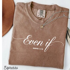 Puede incluir: Camiseta color espresso con las palabras "Even if" y "Daniel 3:18" en escritura blanca. Un collar plateado con un colgante descansa sobre la camiseta. La camiseta tiene una etiqueta Comfort Colors.