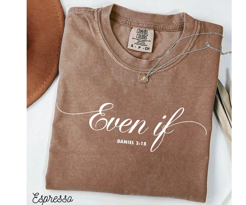 Puede incluir: Camiseta color espresso con las palabras "Even if" y "Daniel 3:18" en escritura blanca. Un collar plateado con un colgante descansa sobre la camiseta. La camiseta tiene una etiqueta Comfort Colors.