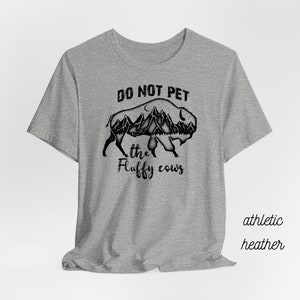 May include: Gray t-shirt with a black graphic of a bison with mountains inside. The text "Do Not Pet the Fluffy Cows" is printed on the shirt.