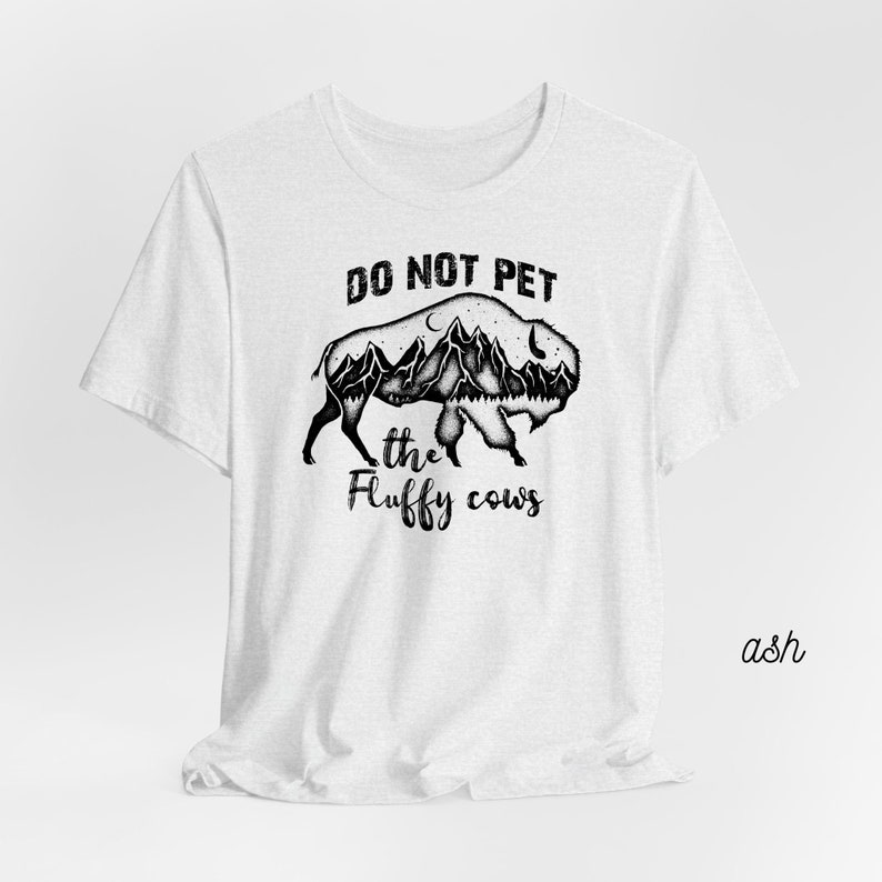 May include: A white t-shirt with a black and white graphic of a buffalo with mountains inside its silhouette. The text "DO NOT PET the fluffy cows" is printed on the shirt.