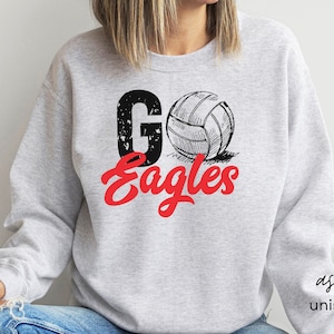 以下が含まれることがあります： グレーのトレーナーに、赤と黒の文字で「Go Eagles」と書かれています。テキストの上に、バレーボールの白黒のイラストがあります。