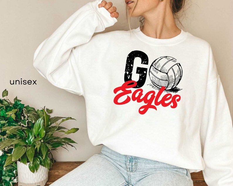 以下が含まれることがあります： 白地に黒と白のバレーボールのグラフィックと赤い文字で「Go Eagles」と書かれたスウェットシャツです。
