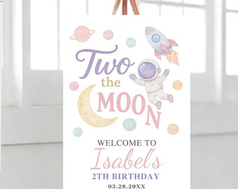 May include: A white sign on a wooden easel with a space-themed design. The sign reads "Two the Moon" with an astronaut, rocket, planets, and moon illustrations. The text "Welcome to Isabel's 2th Birthday" is also displayed.