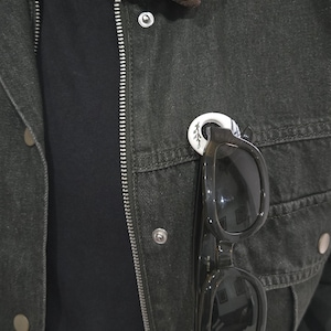 May include: Dark green denim jacket with a brown corduroy collar. Black sunglasses are clipped to the jacket with a white and black decorative pin. The jacket has a zip and snap closures.