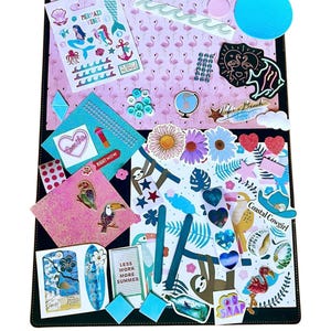 Può includere: Una pagina di scrapbook decorativa con bordo nero, con adesivi a tema sirene, fenicotteri e tropicali. Include adesivi con testo come "Mermaid Vibes", "Right Now" e "Less Work More Summer". Lo sfondo è rosa con motivi di fenicotteri.