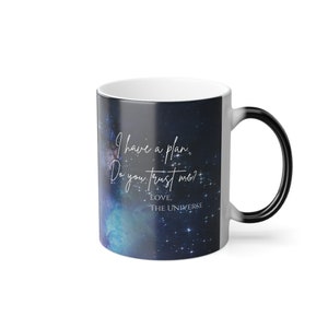 Puede incluir: Taza de cerámica blanca con asa y borde negros. La taza presenta un diseño de galaxia con el texto "I have a plan. Do you trust me? Love, The Universe" en escritura blanca. La taza está diseñada para cambiar de color.