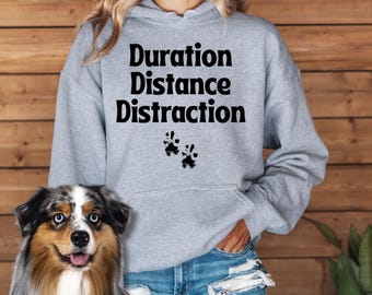 May include: A gray hoodie with the text "Duration Distance Distraction" and paw prints in black. The hoodie is being worn by a person with a dog.