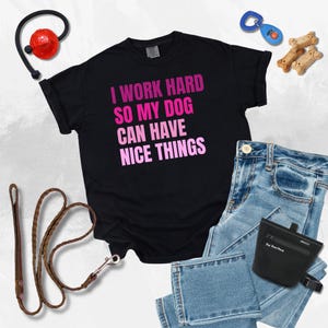 May include: Black t-shirt with pink text that reads "I work hard so my dog can have nice things".